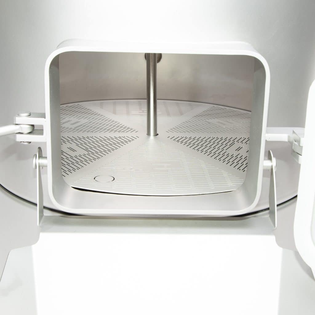 Interior view of a stainless steel cabinet or autoclave with perforated rack and a central vertical support rod beneath a rounded opening