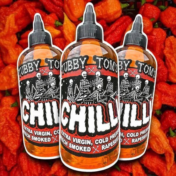 Three hot sauce bottles with skull-and-skeleton artwork on bold red-and-black labels placed in front of a background of red chilies.
