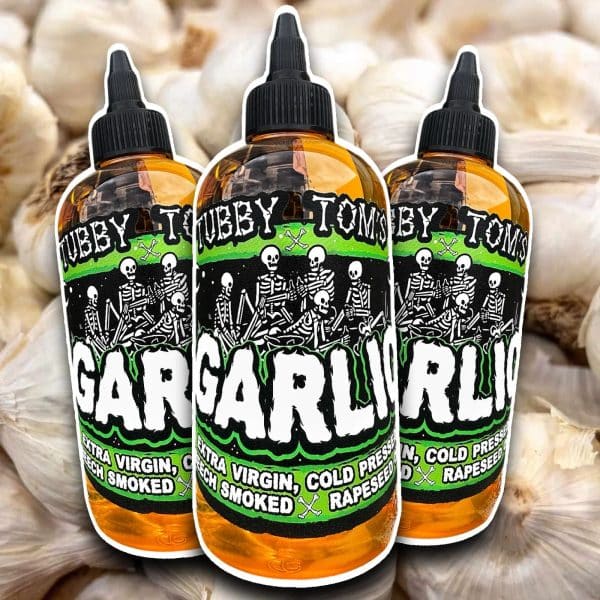 Three amber dropper bottles with skull-and-skeleton artwork on a green label, set against a background of garlic bulbs.